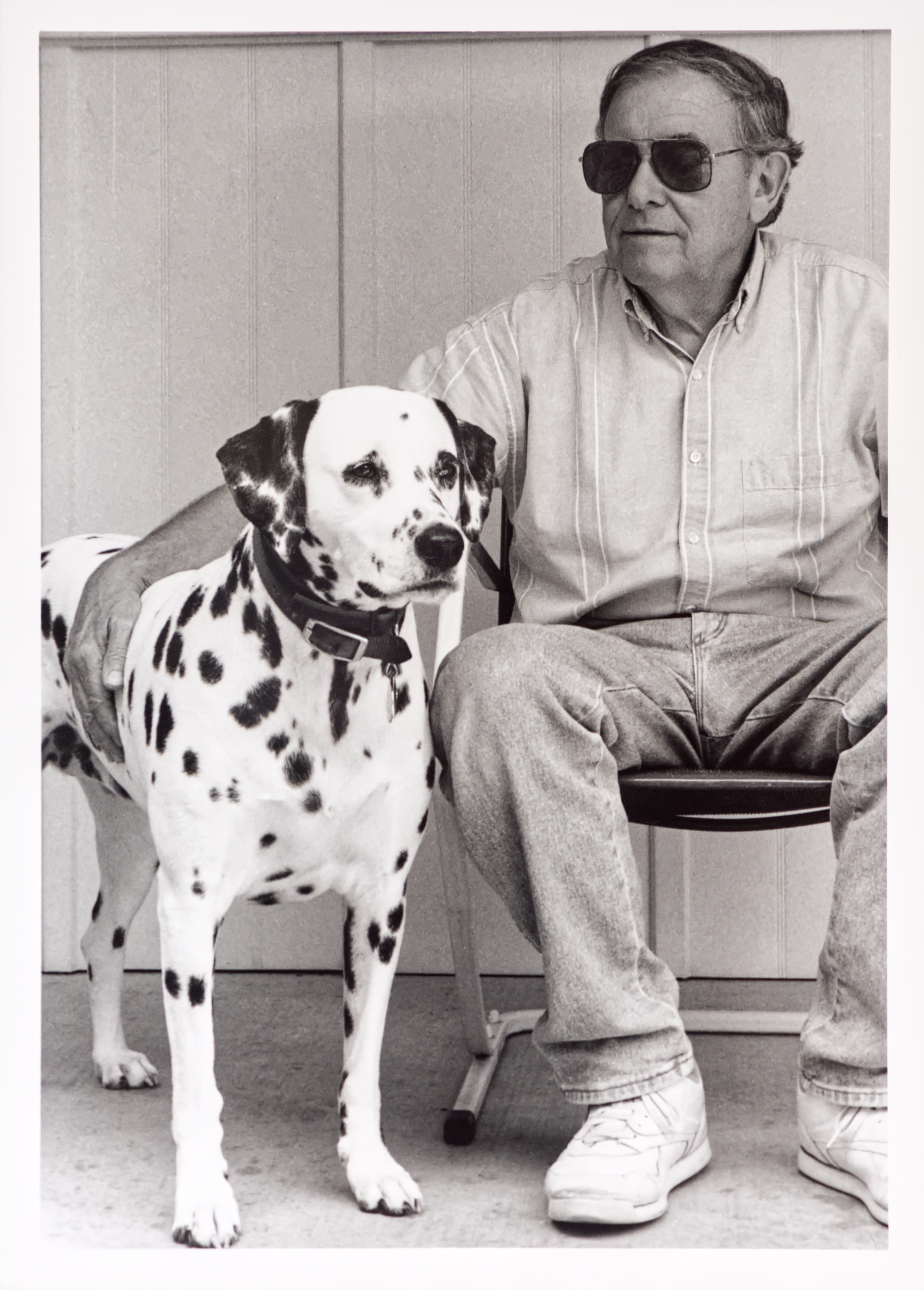 An older man sitting on a porch with his Dalmatian. 