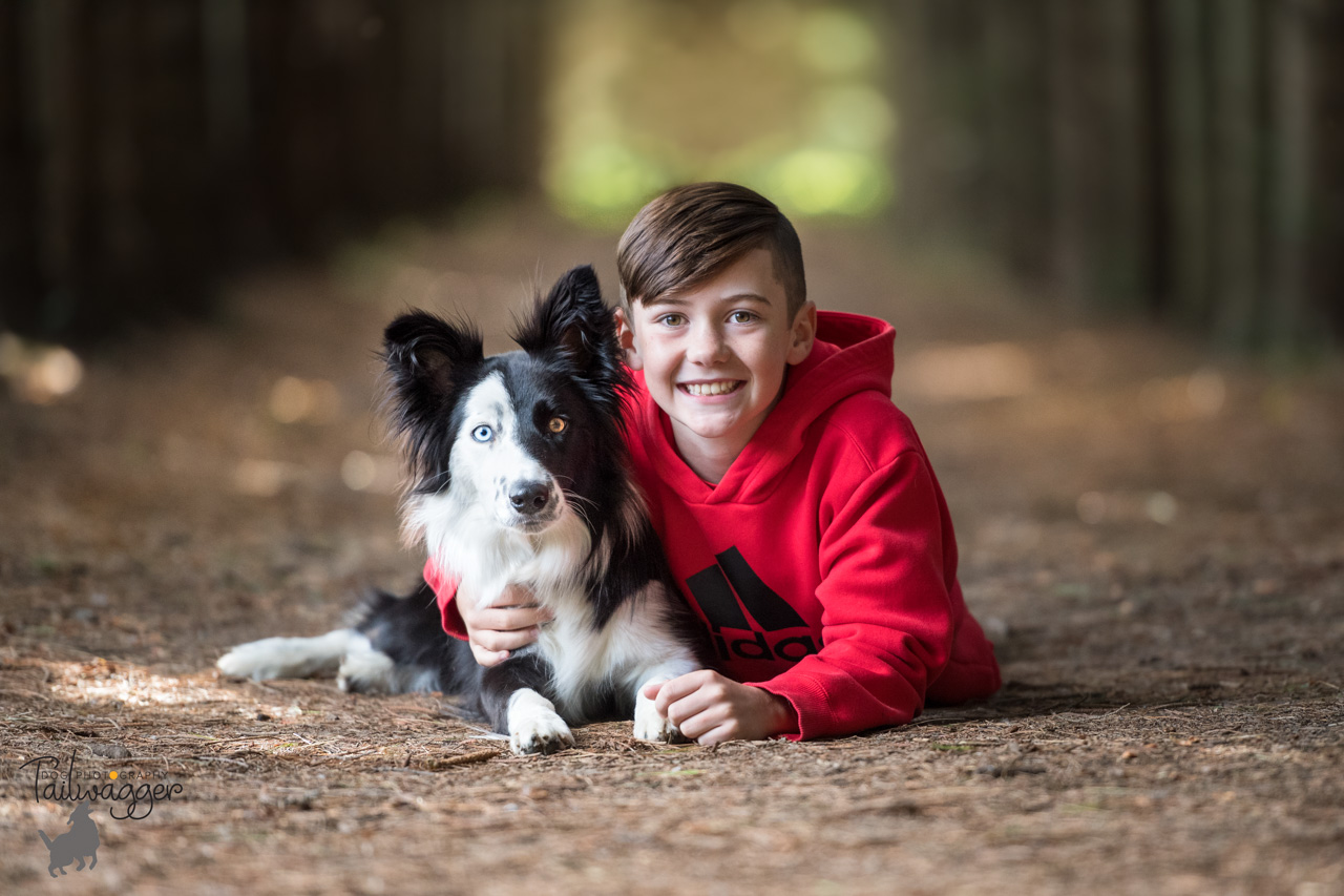 A boy and his border collie lying on the forest floor.