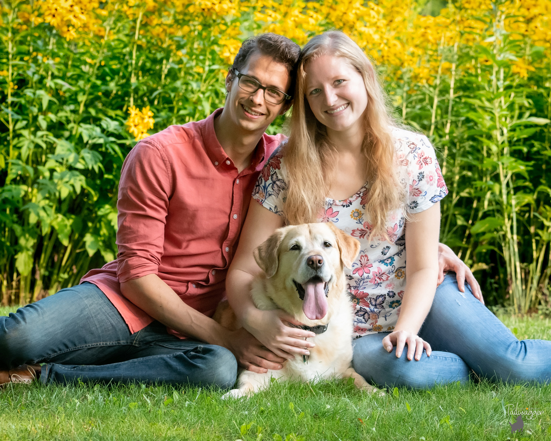 A man, woman and their yellow lab sitting on the grass. 