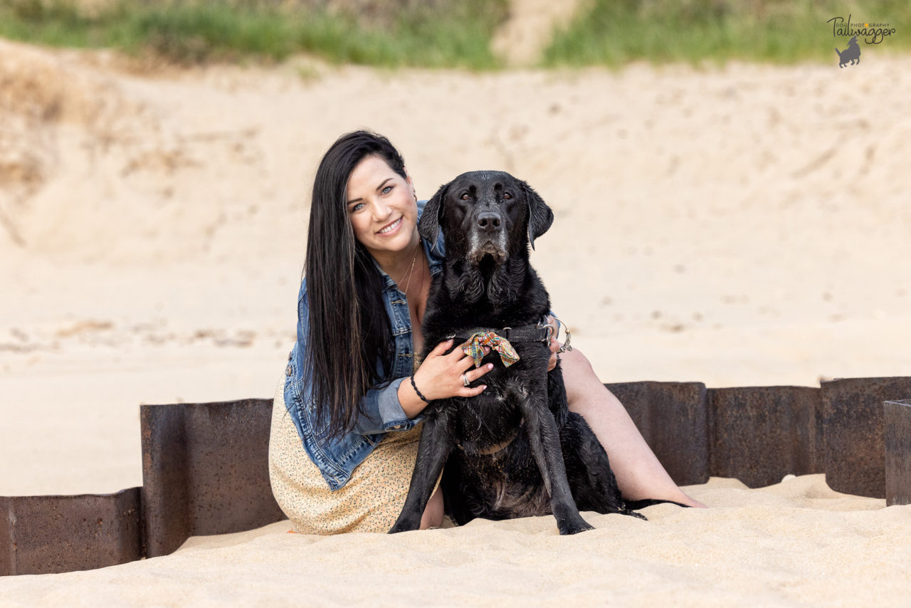 A woman her male black Lab sit in the sand of Lake Michigan in Muskegon, MI.