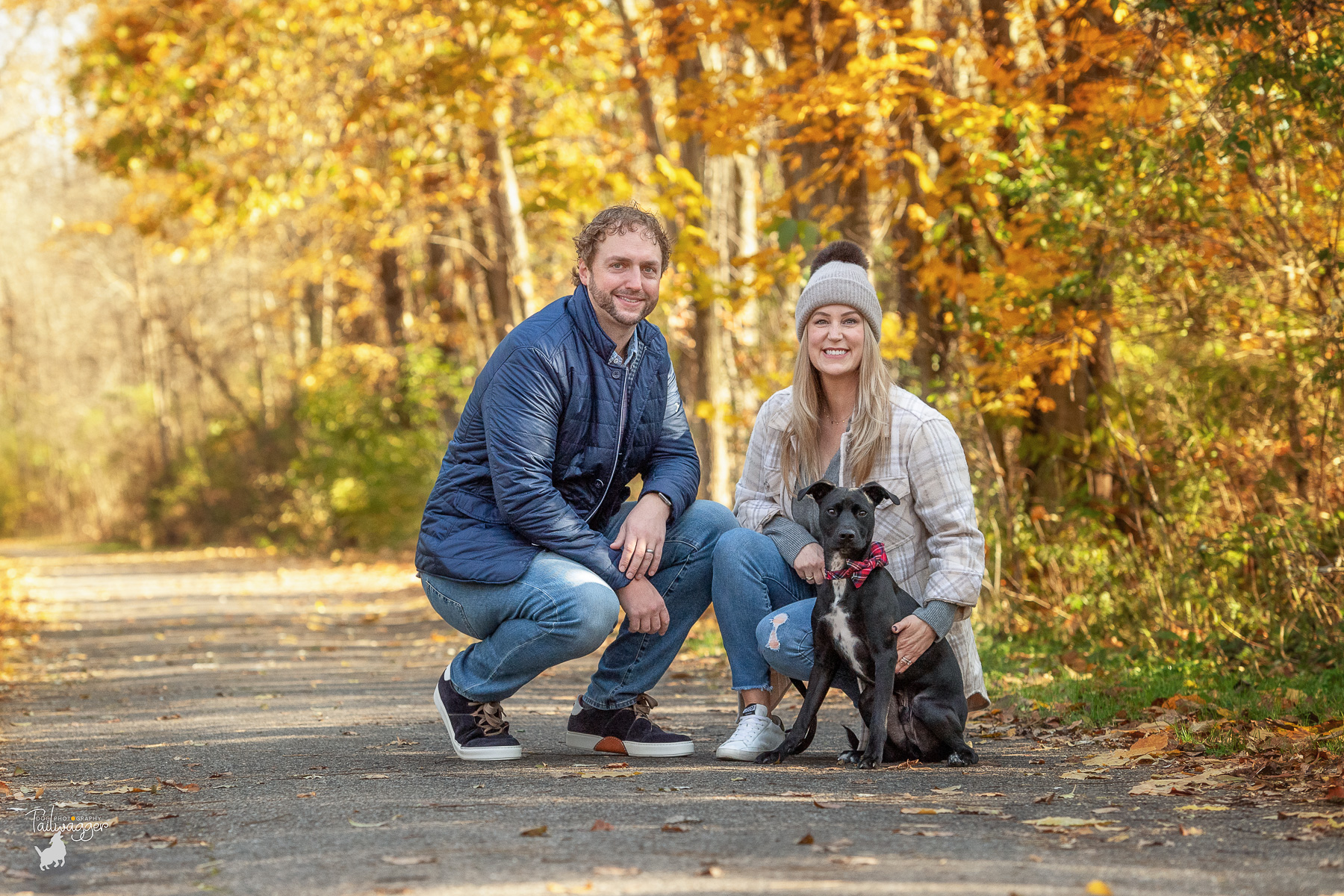 A man and woman crouch down next to their black and white dog to be photographed in Rockford, MI.